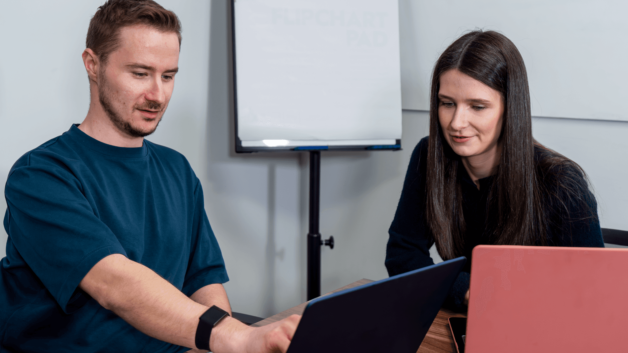 Two colleagues collaborating and looking at a laptop screen in a professional office setting.